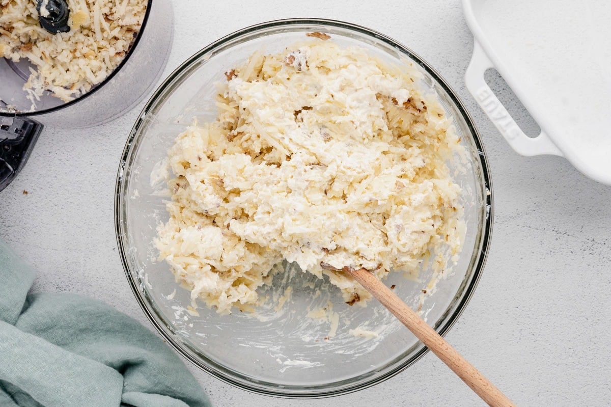 Shredded potatoes, cheese and sour cream mixed together in a glass bowl.