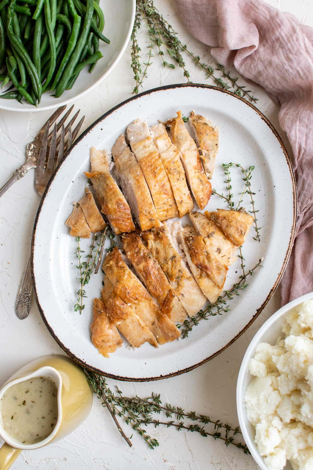 Sliced turkey breast with skin on a platter with fresh thyme.