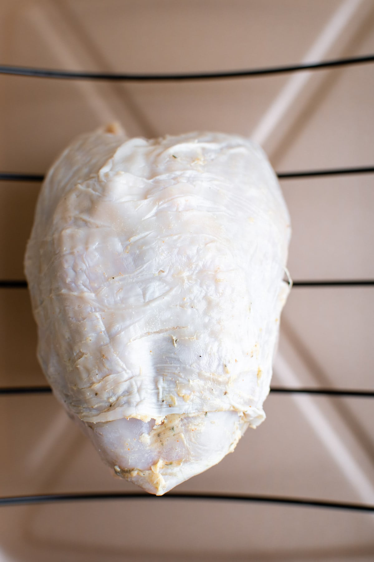 Whole uncooked turkey breast on a rack in a pan.