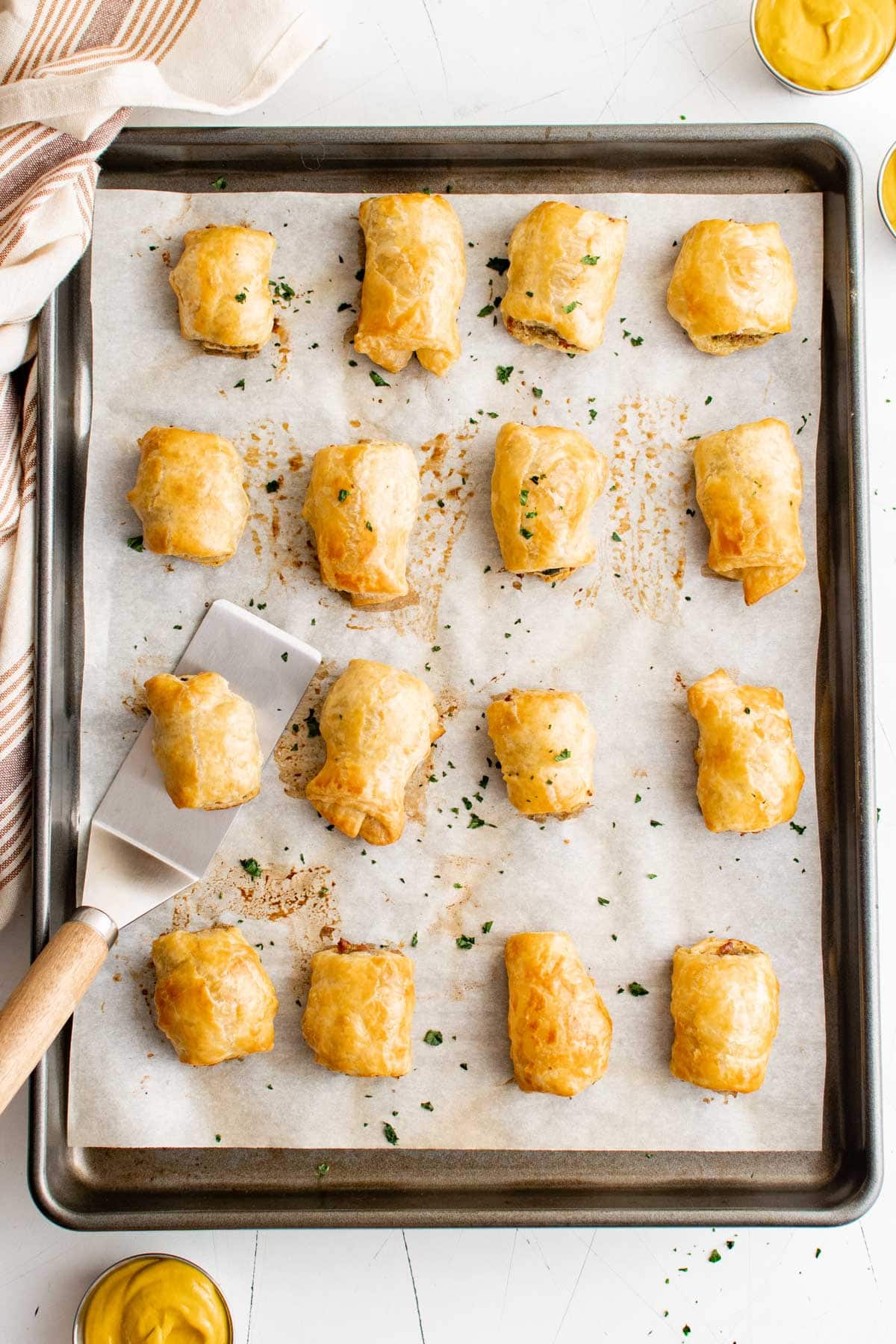 Sheet pan with sausage rolls and a spatula.