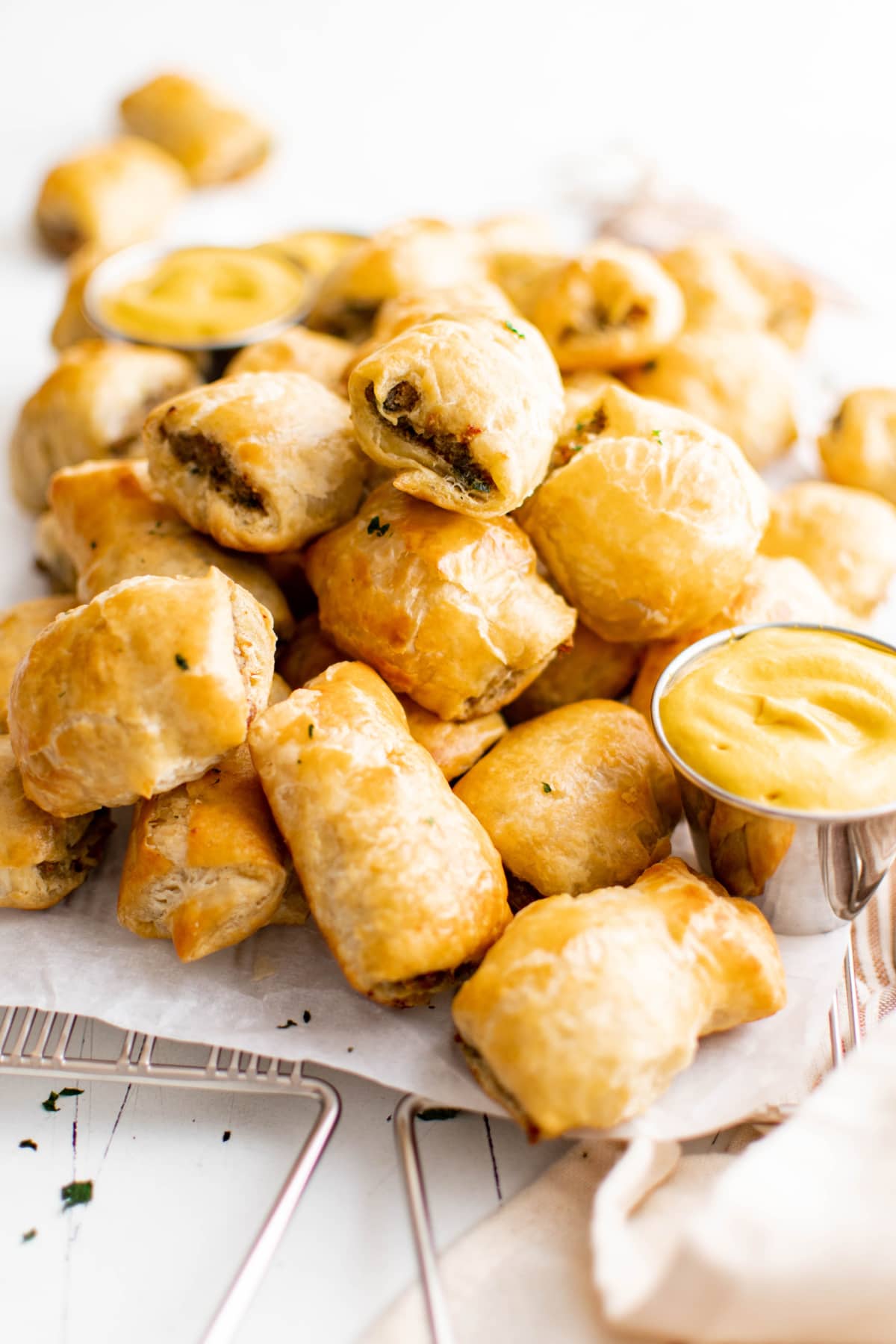 Piles of sausage rolls stacked on a white platter with a small dish of mustard