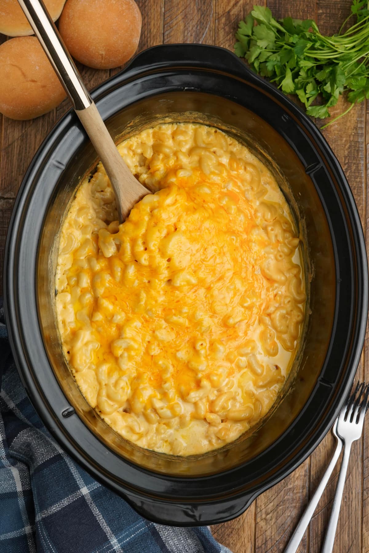 Slow cooker pot with creamy mac and cheese and a wooden spoon.