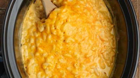 Slow cooker pot with creamy mac and cheese and a wooden spoon.