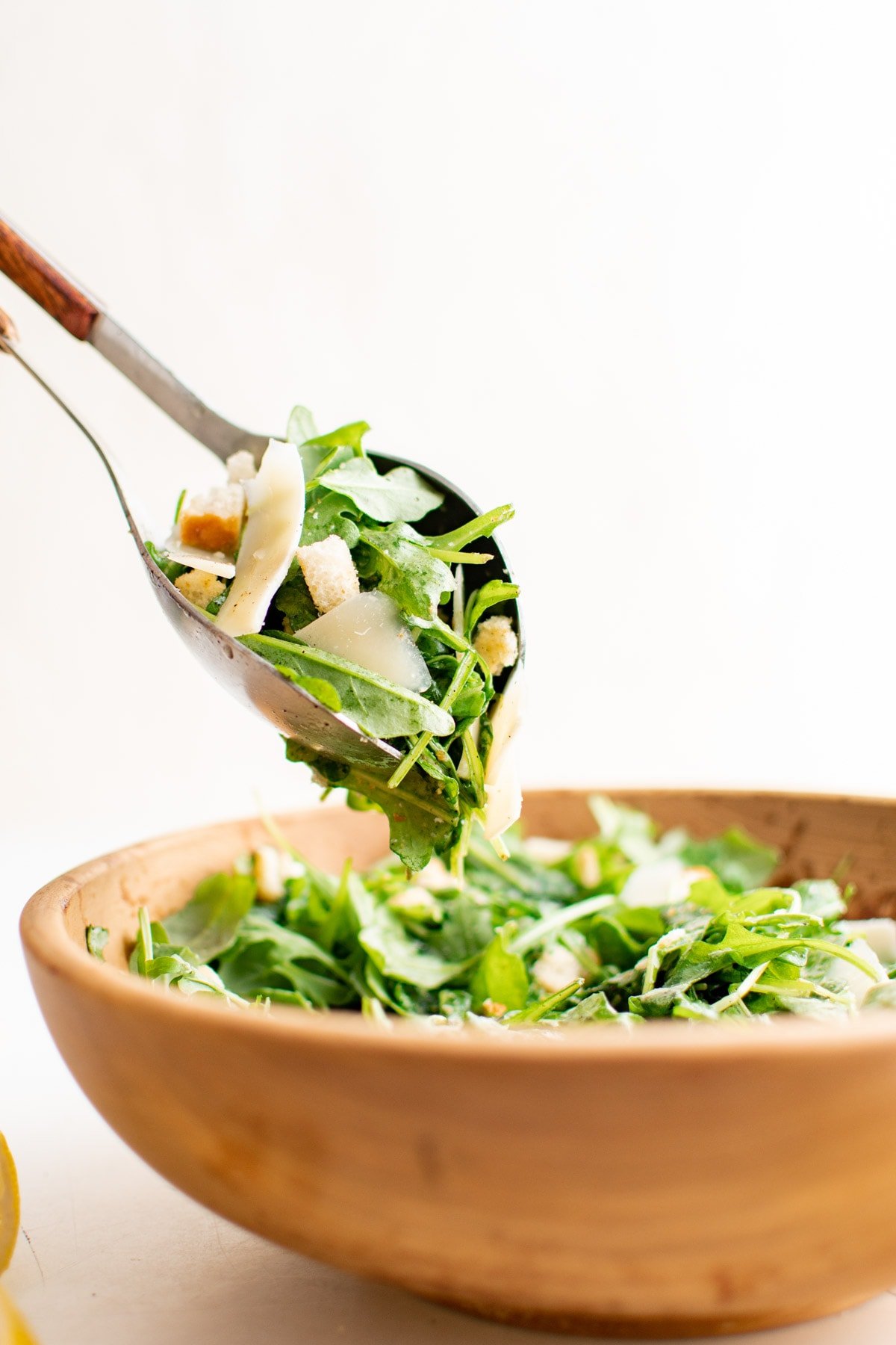 Arugula salad with salad tongs in a wooden bowl