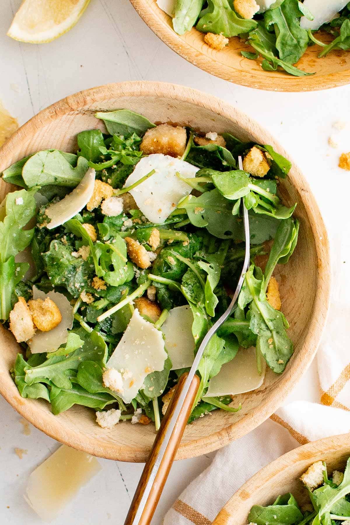 Arugula leaves, parmesan and croutons i a wooden bowl with salad tongs.