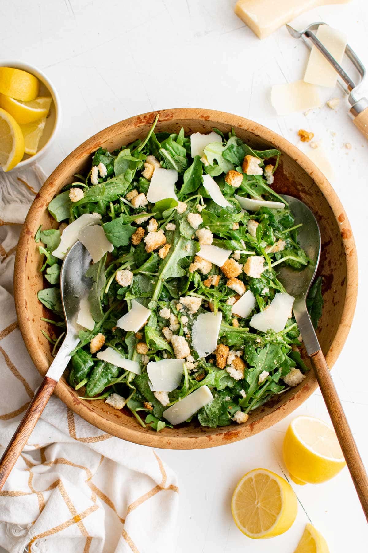 Arugula, Parmesan cheese, crouton in a wooden bowl with salad tongs.