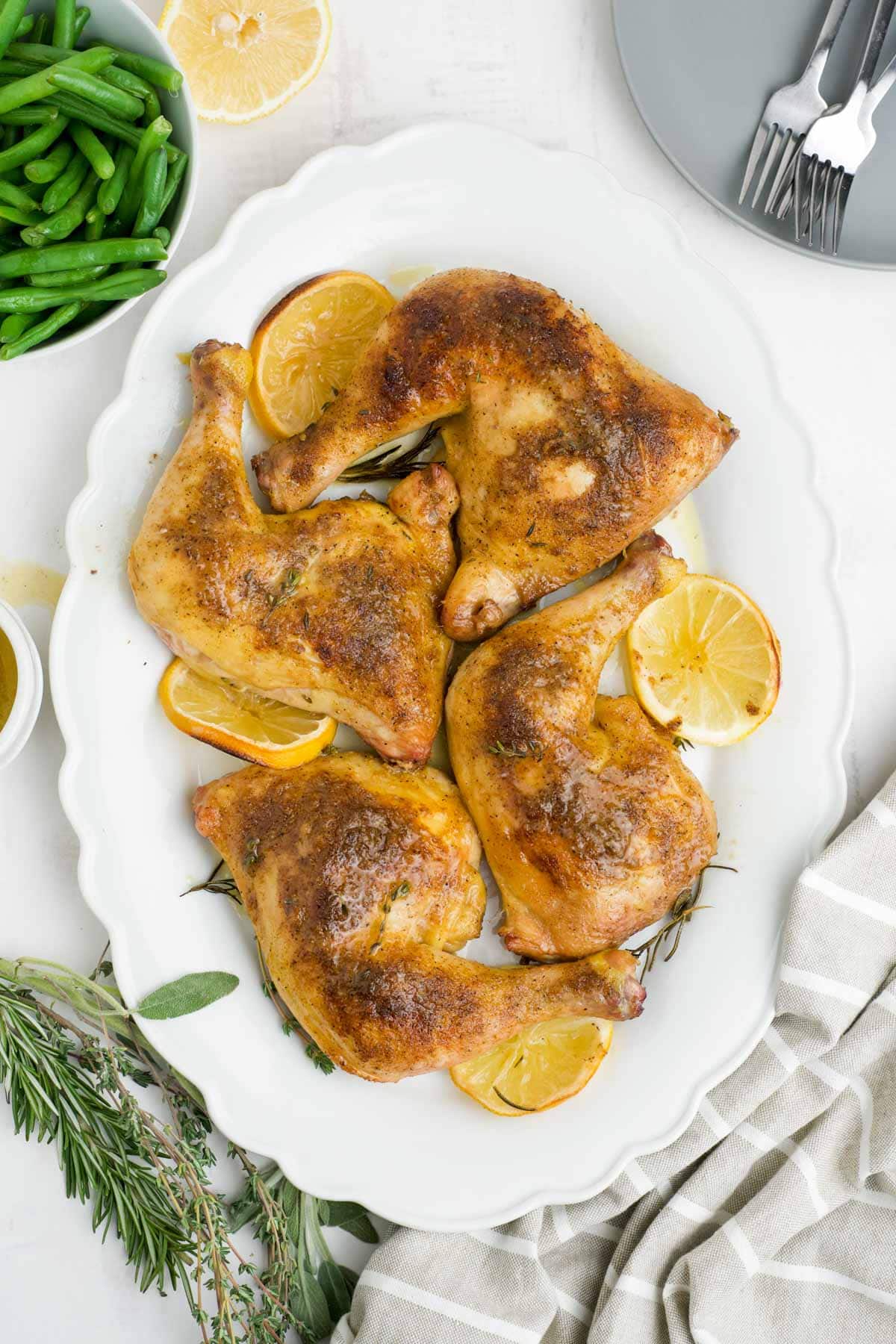 White platter with roasted chicken legs and lemon slices.