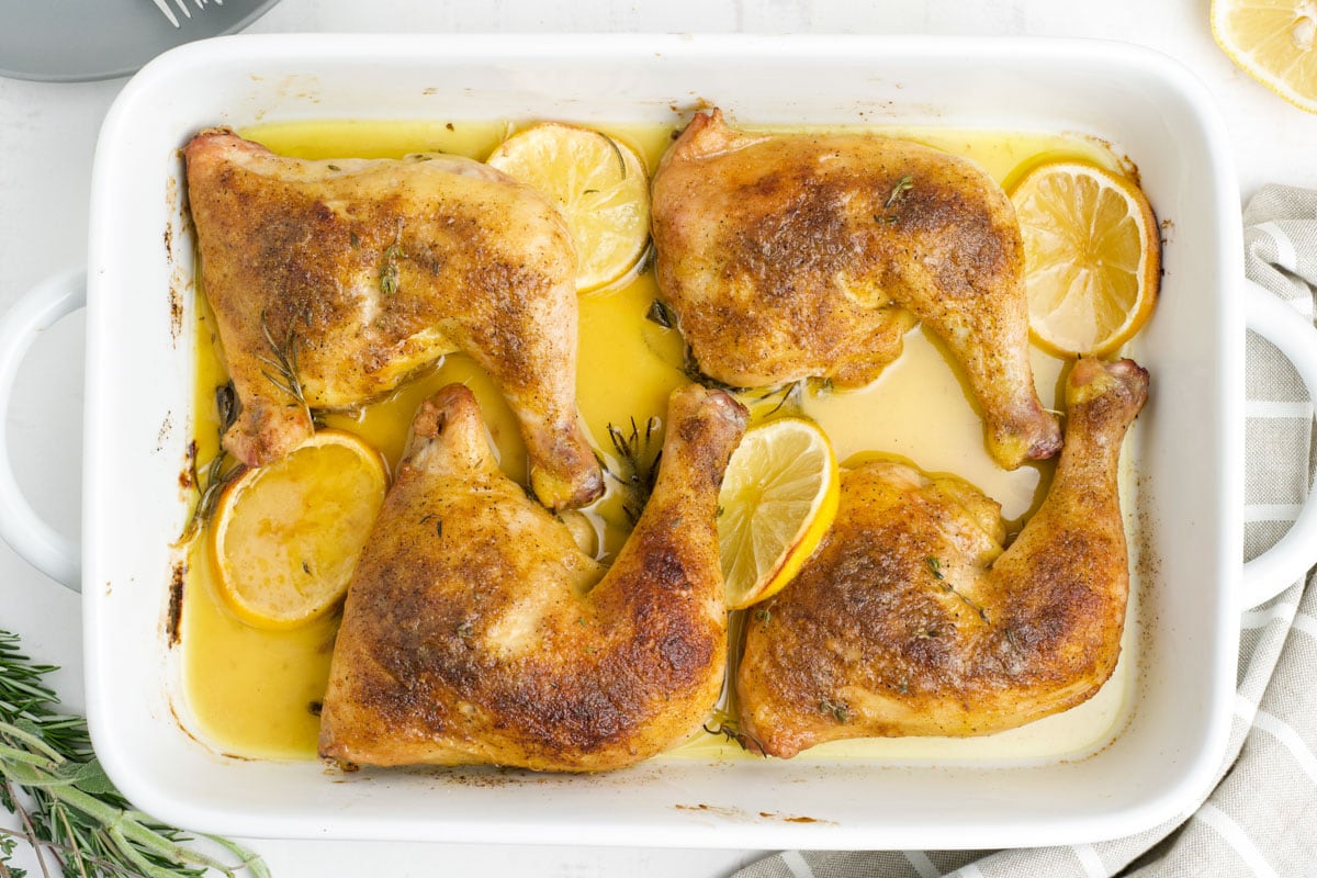 Roasted chicken legs in a baking dish with lemon slices.