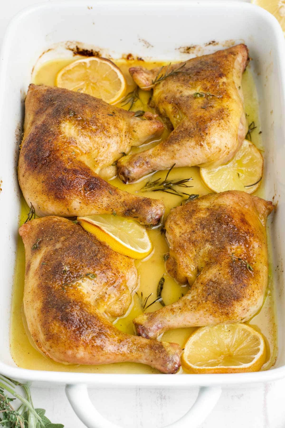 Chicken leg quarters in a white baking dish with lemon slices.