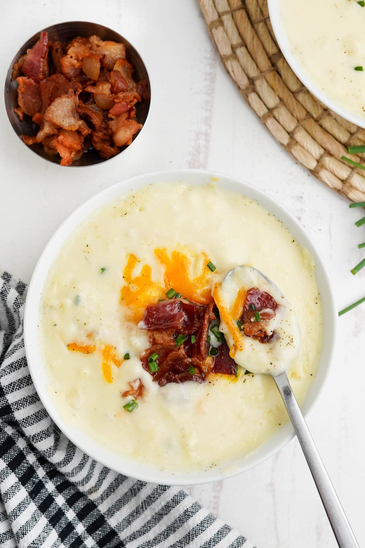 Potato soup in a bowl topped with bacon, cheese and chives.