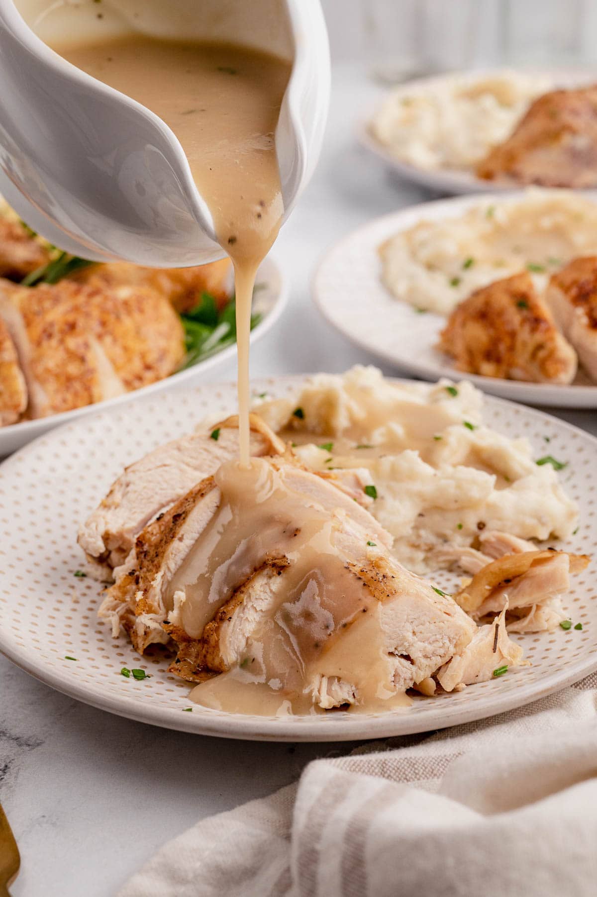 Sliced chicken breast and mashed potatoes on a white plate, a gravy boat pouring gravy over the chicken.