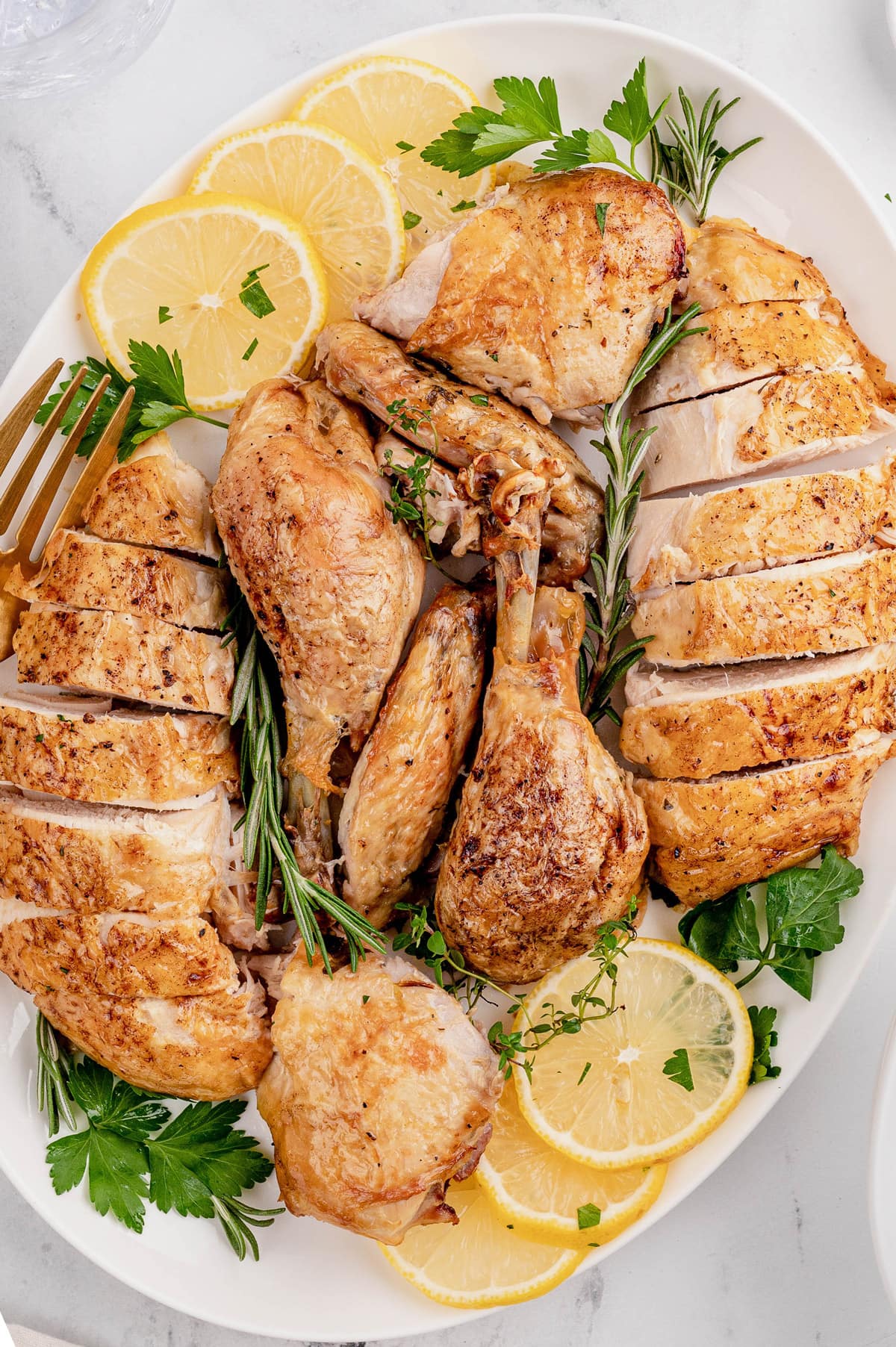 Carved chicken on a white platter with sliced lemons and fresh herbs.