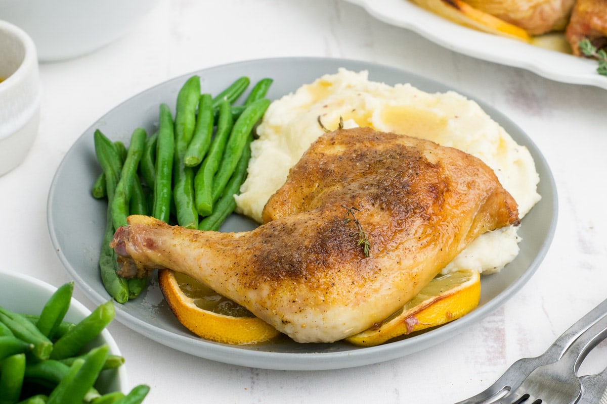 Chicken leg quarter, mashed potatoes and green beans on a gray plate.