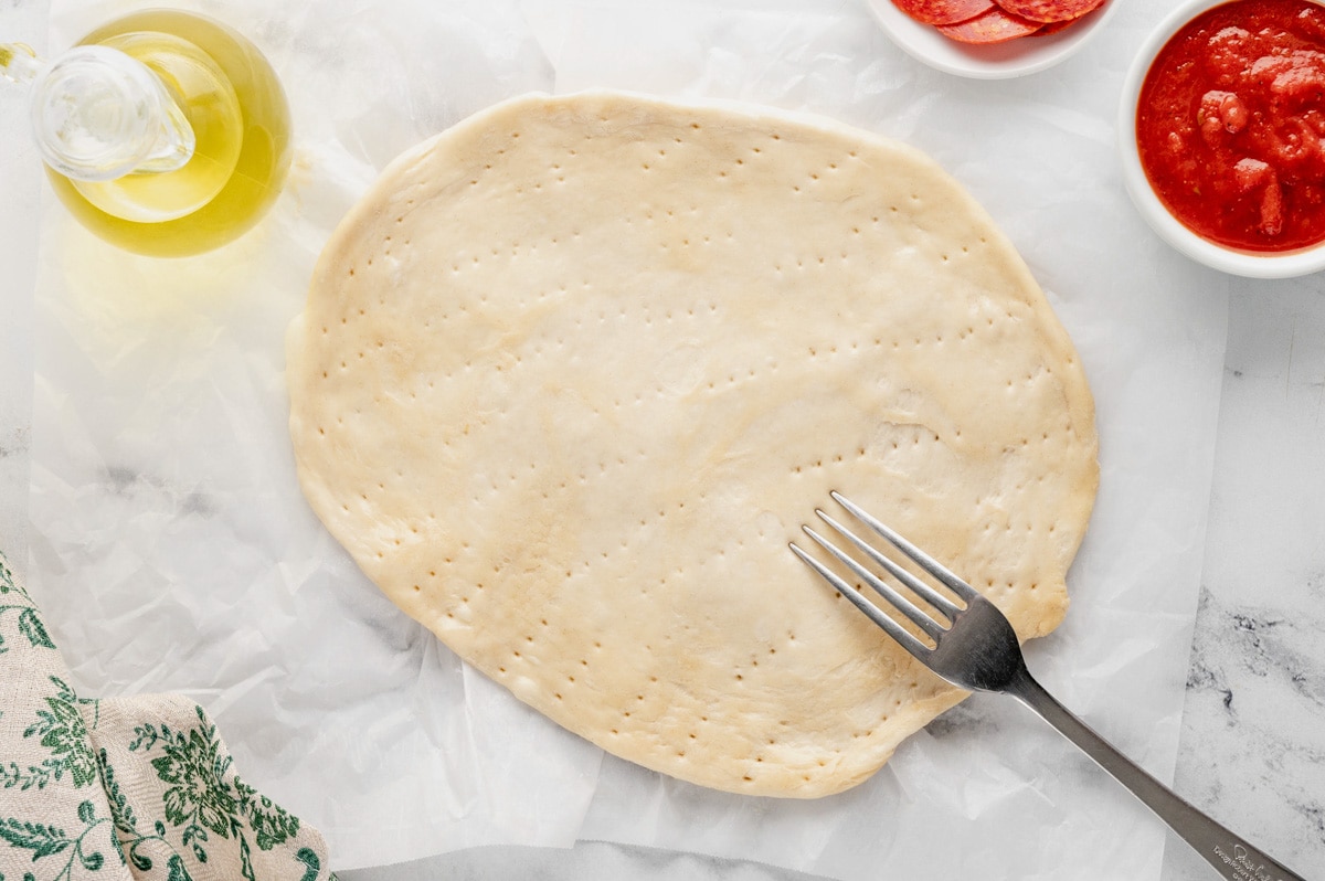 Fork poked holes into a round of pizza dough.