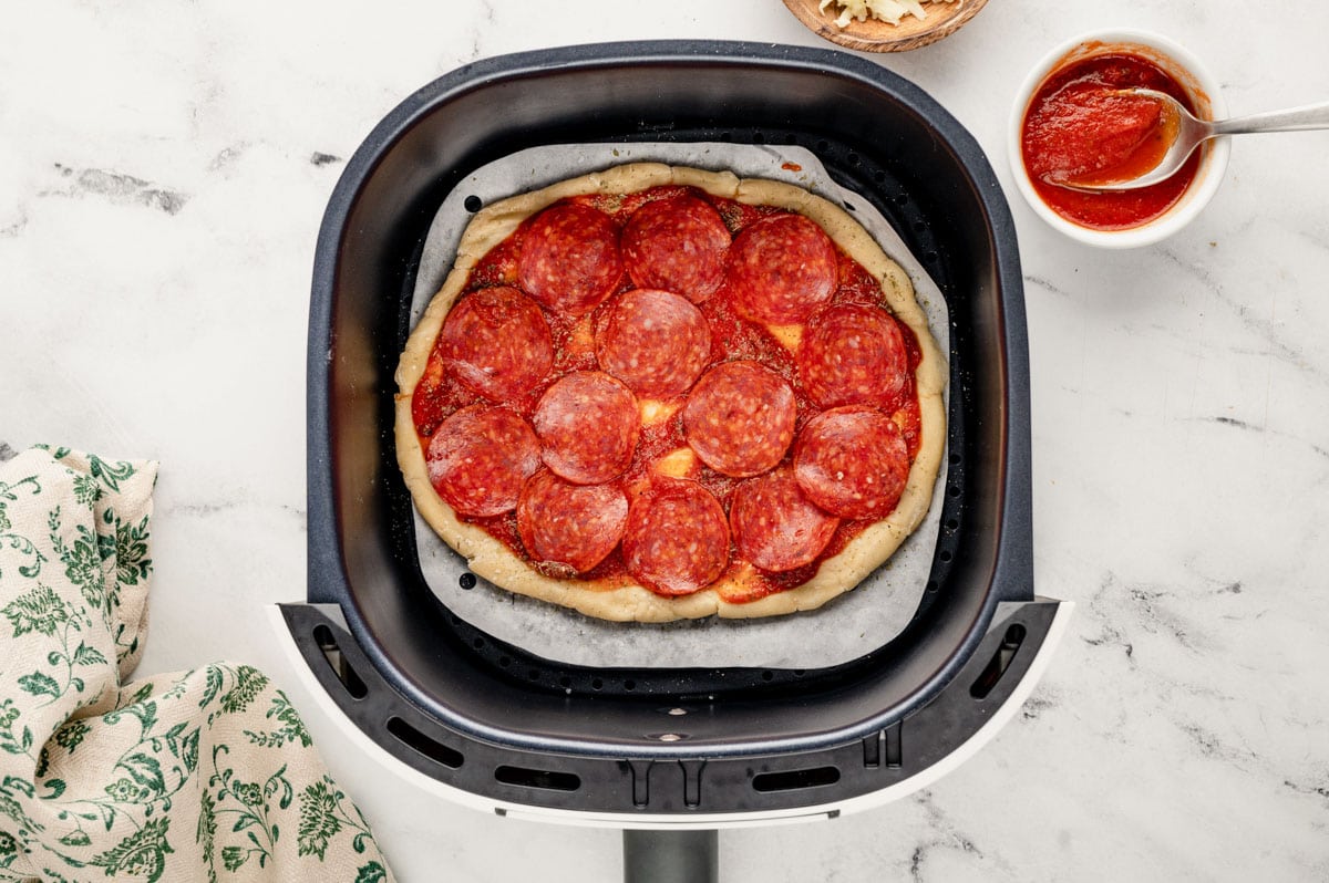 Pizza dough with pizza sauce and pepperoni in an air fryer.
