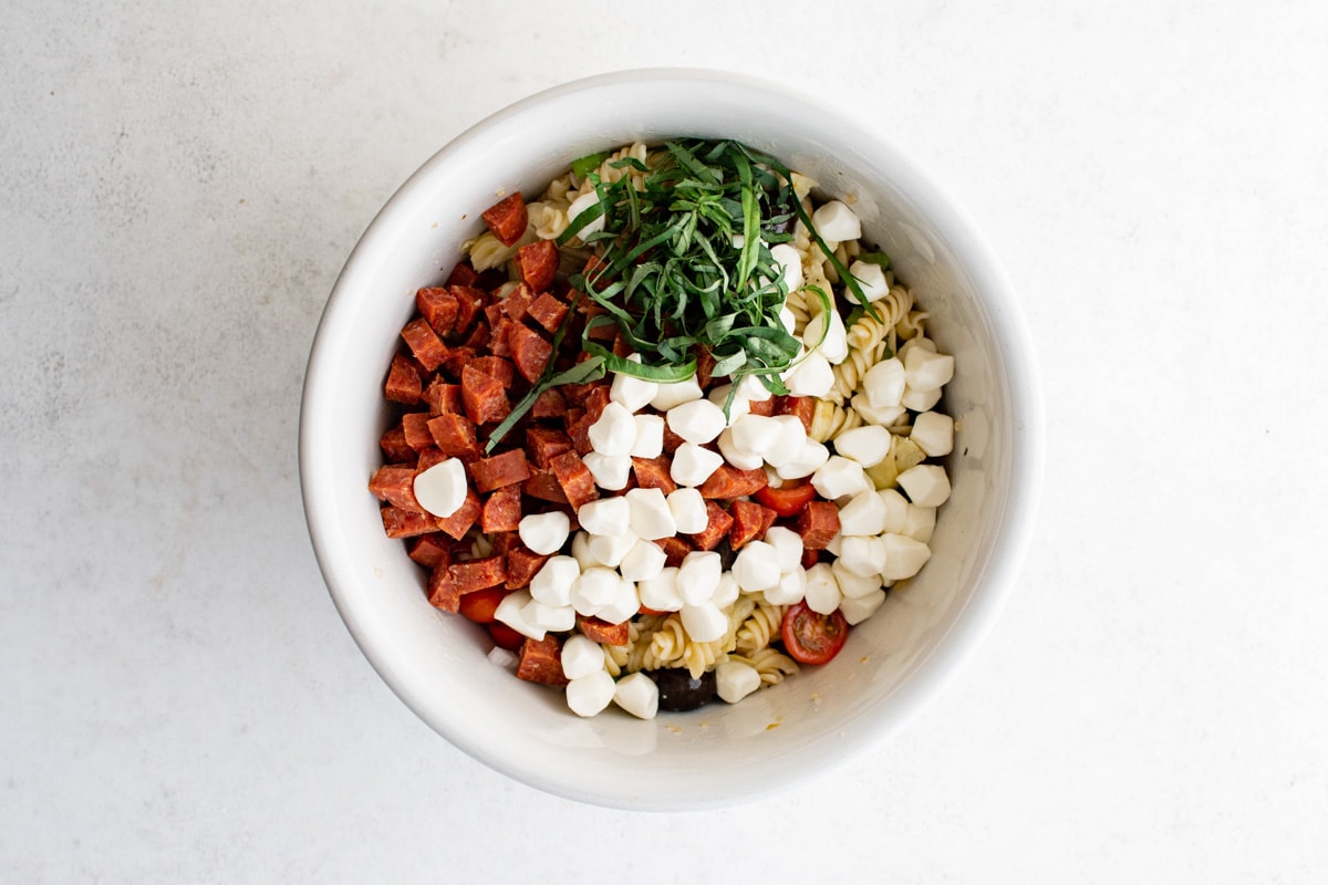 Mozzarella pearls, diced tomatoes, basil and pasta in a bowl.