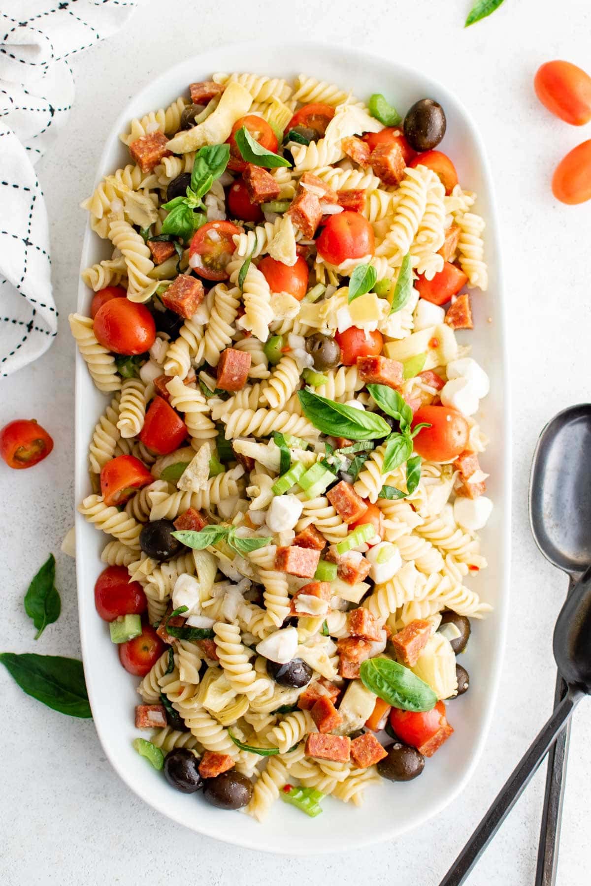 Rotini pasta, tomatoes, olives, cheese and salami in hte form of a pasta salad on a large platter.