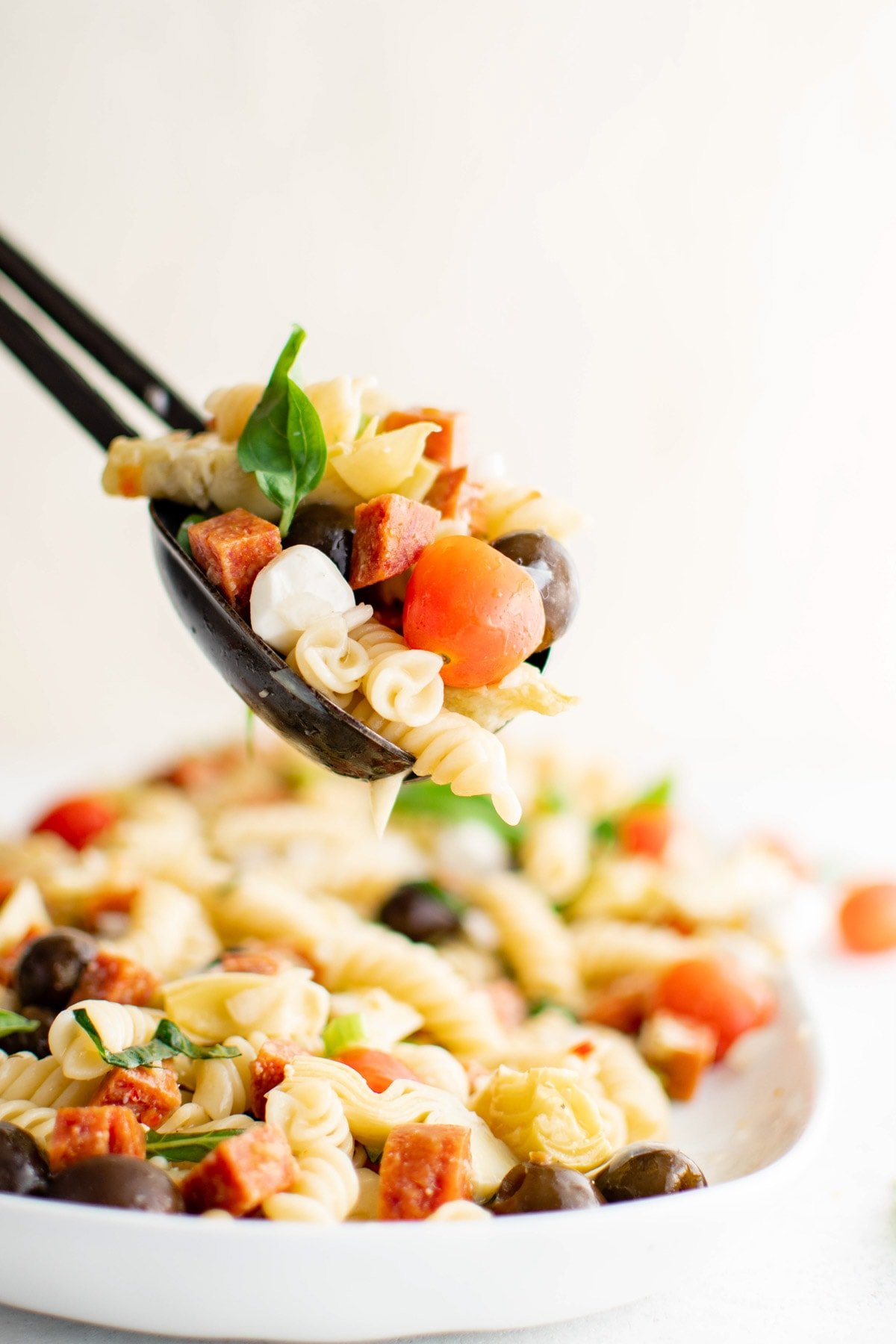 Pasta salad in a bowl and lifted with tongs.