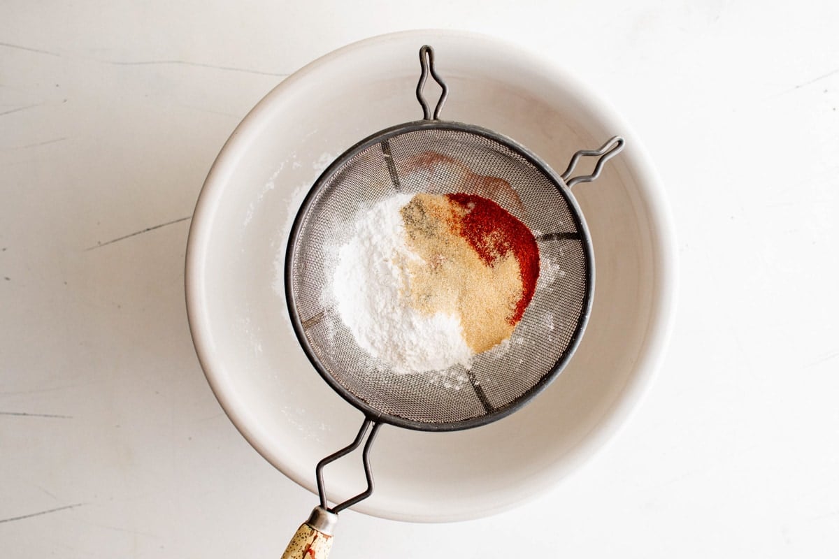 Flour and seasonings being sifted in a bowl.