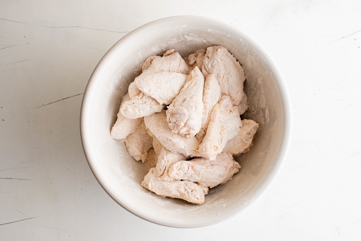 Chicken wings in a bowl, coated with flour and spices.