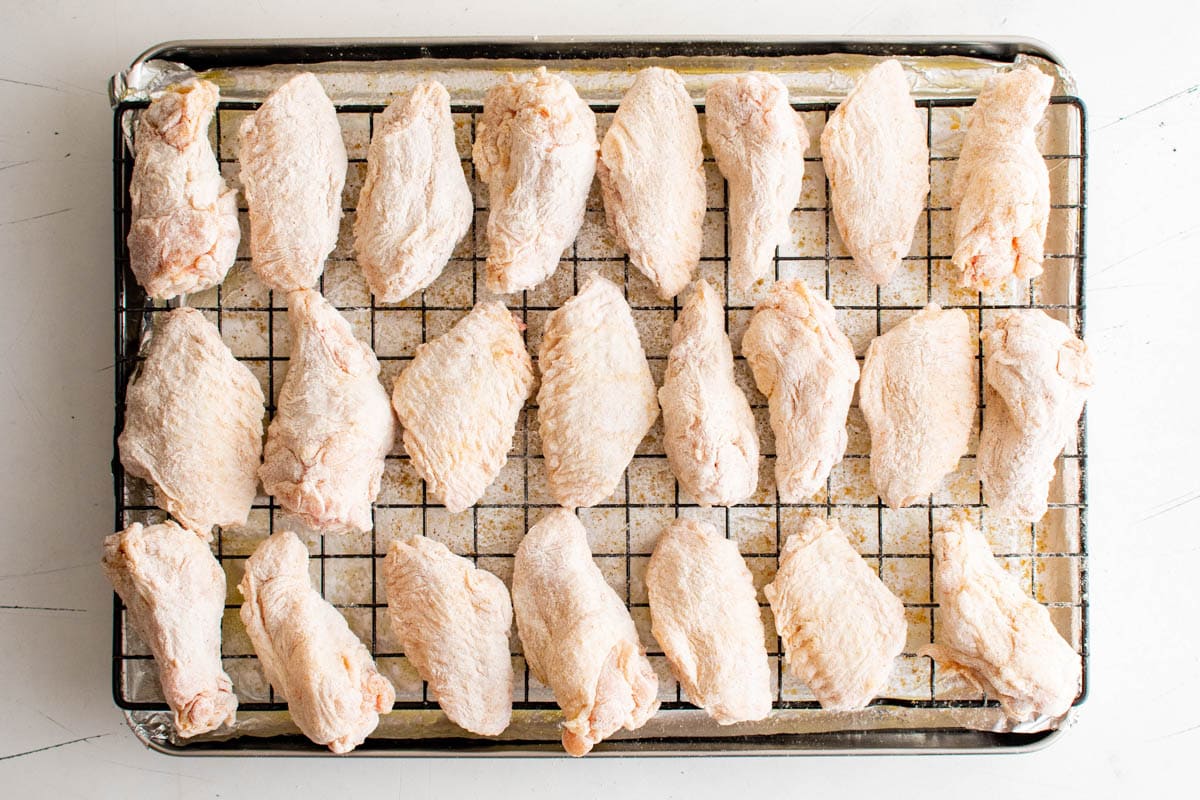 Seasoned and floured wings on a baking rack over a baking sheet.