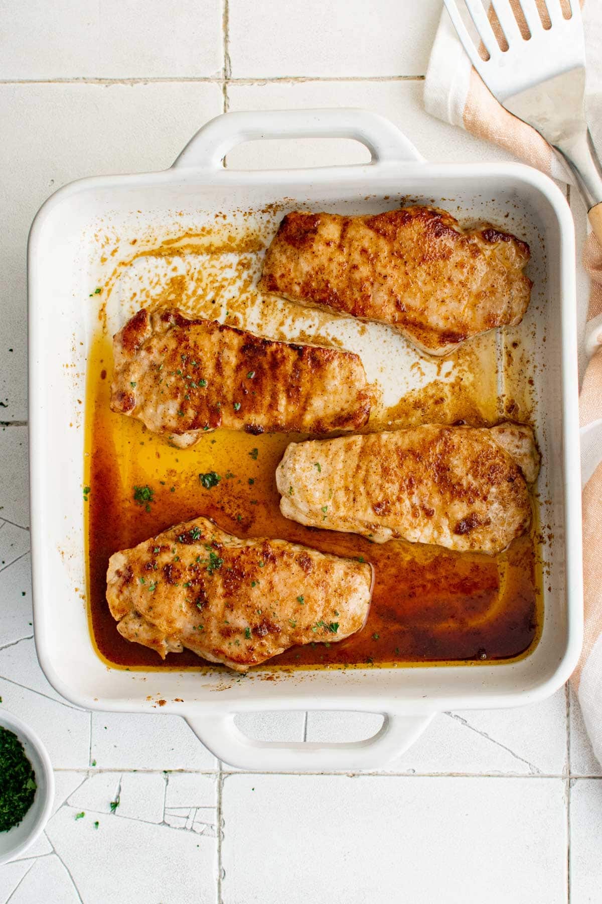 Baked pork chops in a white baking dish.