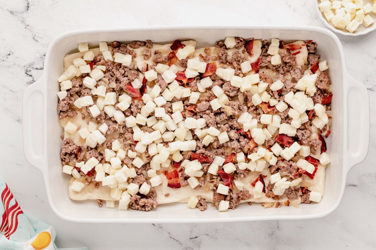 Sausage and potatoes over cut up biscuits in a baking dish.