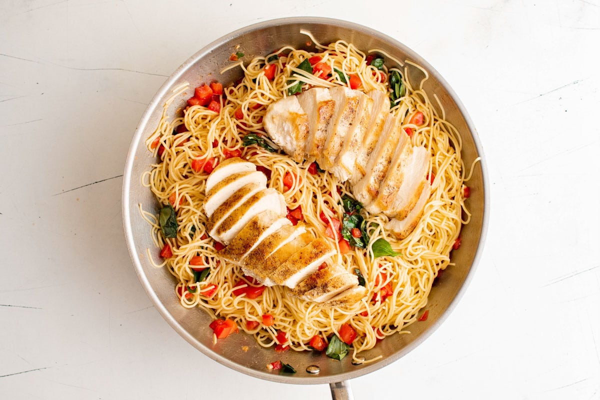 Sliced chicken breast over pasta with tomatoes.