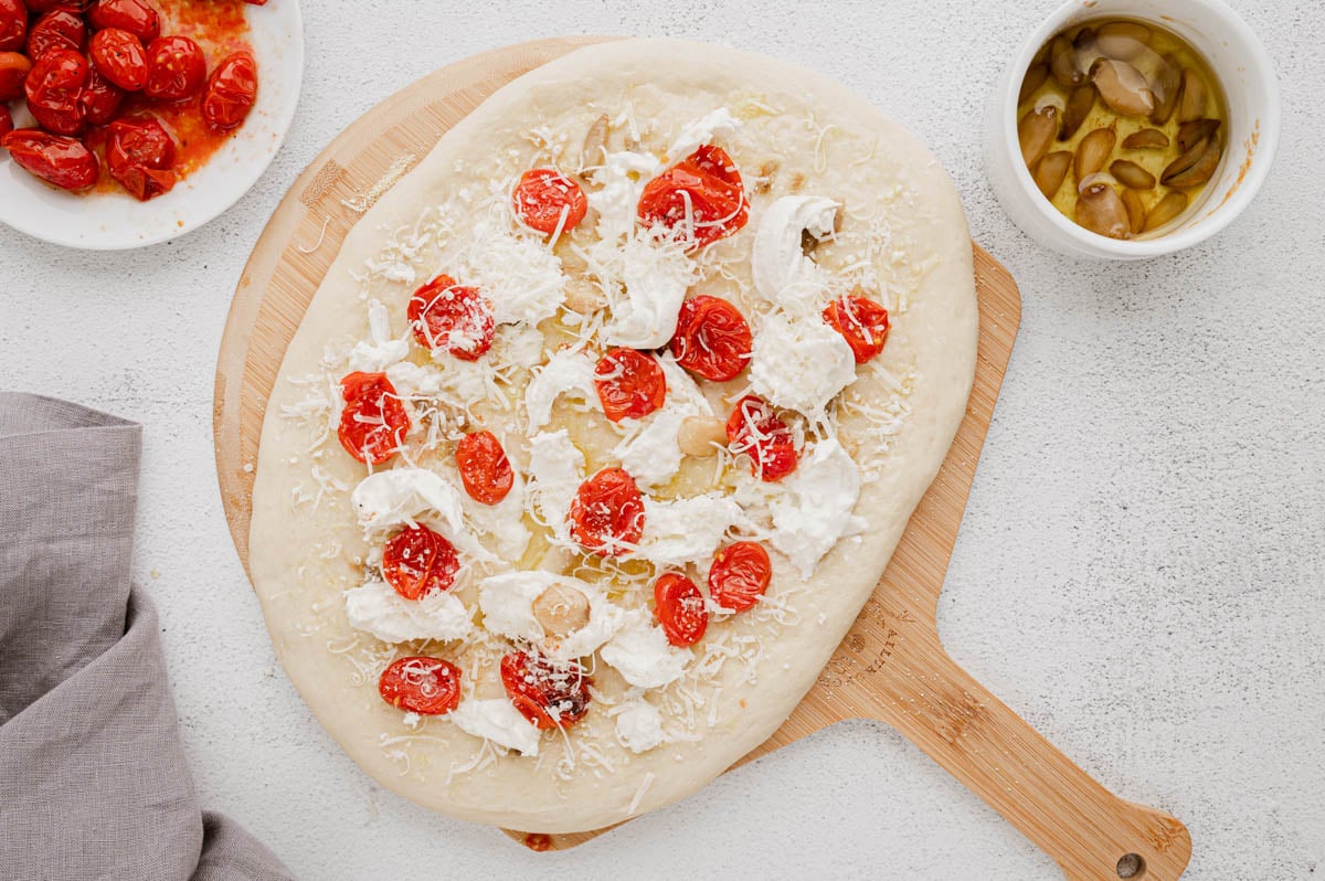 Stretched out pizza dough topped with burrata, tomatoes, and cheese.