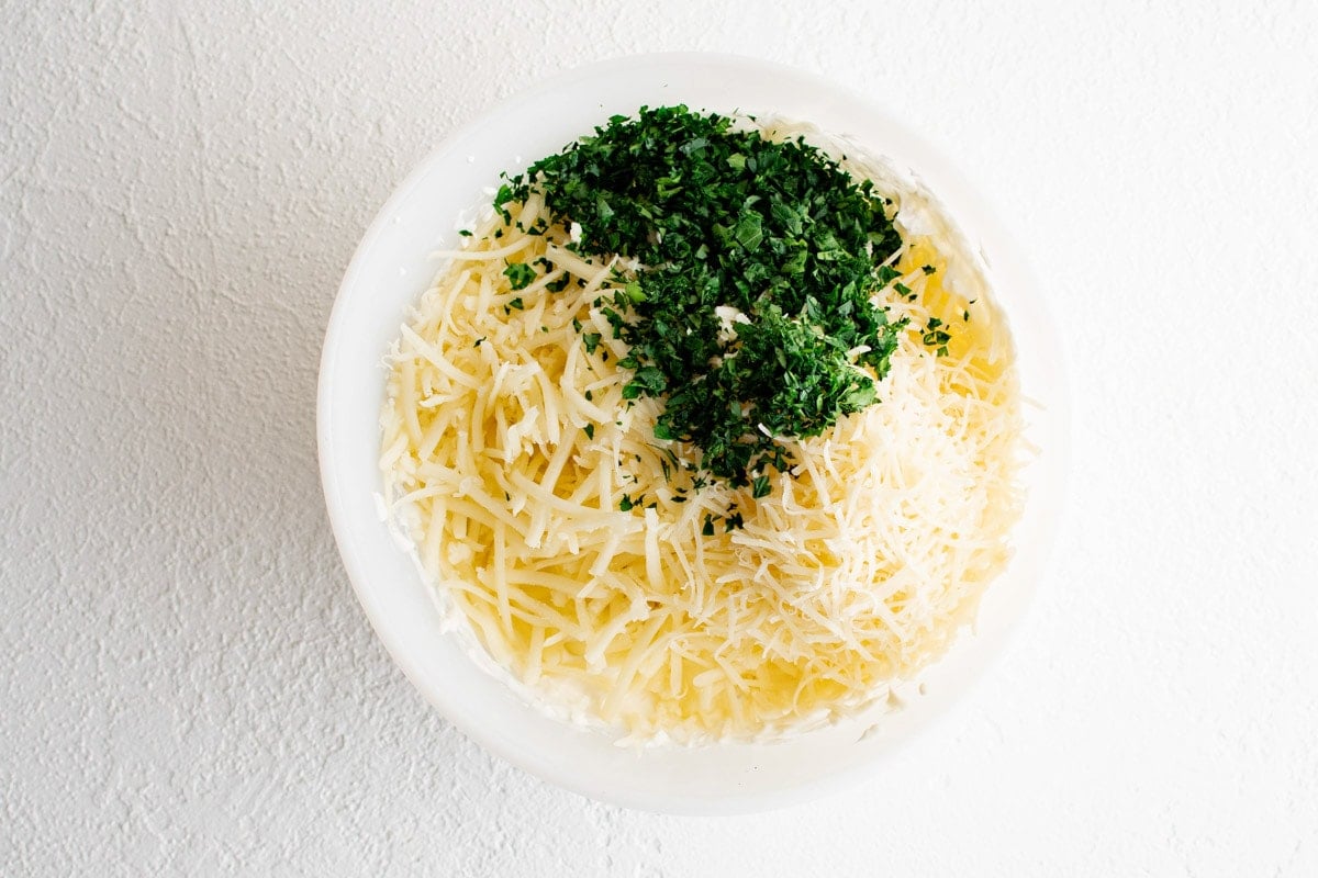 Shredded cheeses and minced parsley in a bowl.