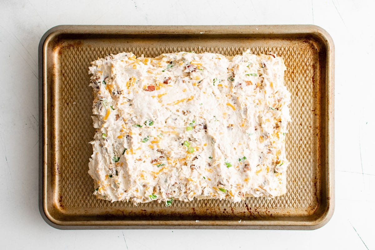 The bottom half of a slab of rolls with a creamy chicken mixture spread on top.