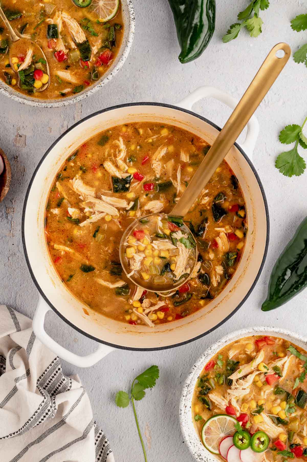 Chicken Poblano Soup in a pot with bowls of soup, a ladle and spoons.