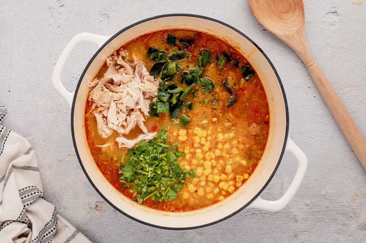 Broth in a pot with corn, chicken, cilantro and green onion.