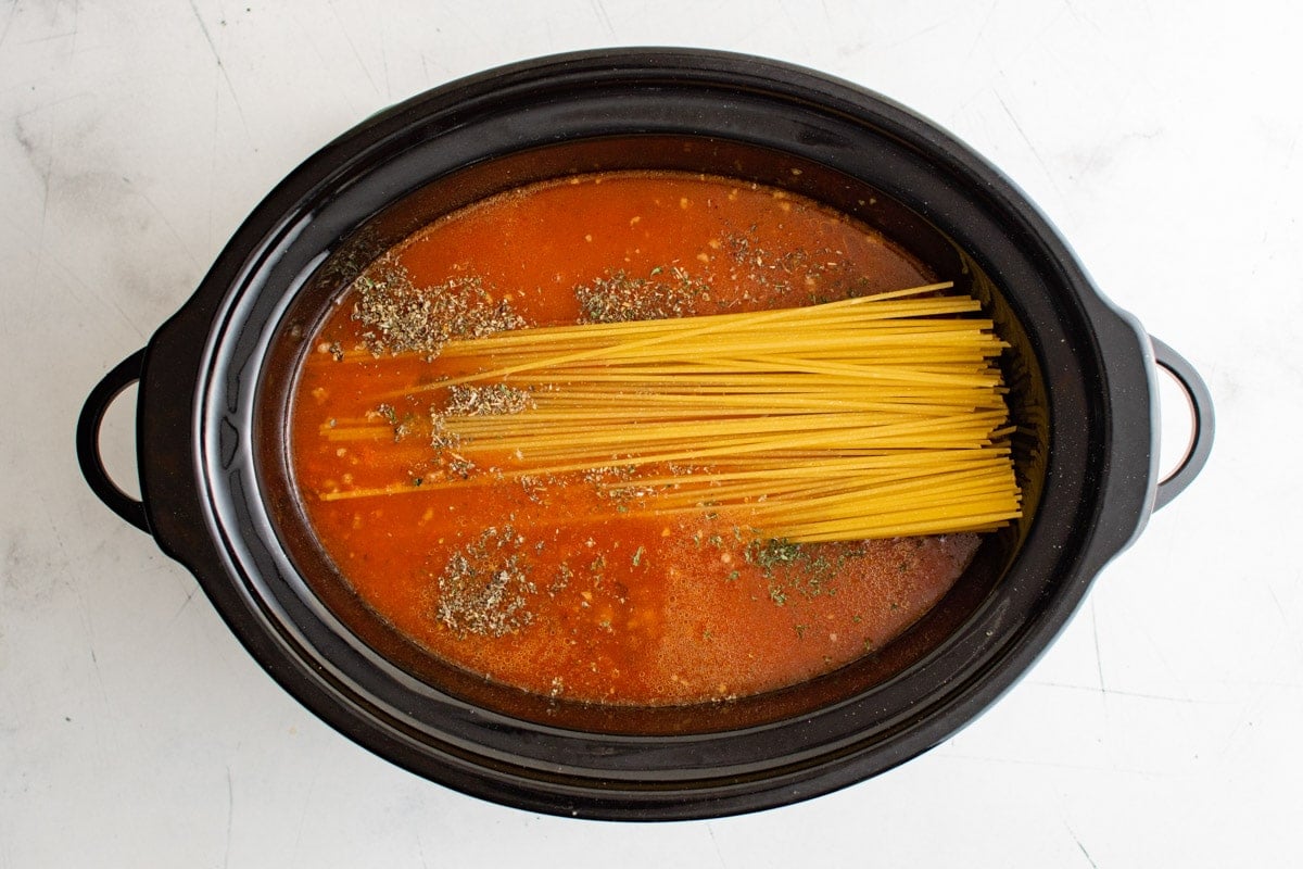 Slow Cooker pot with sauce and dry noodles.