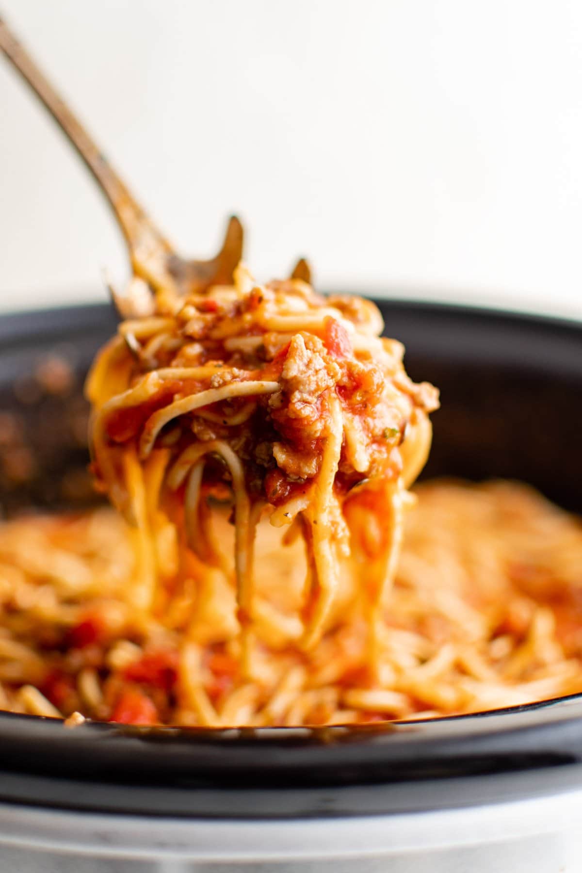 Spaghetti lifted from a crockpot with a large serving spoon.