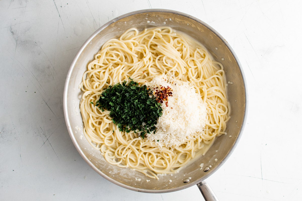 Spaghetti in a skillet with minced parsley and parmesan cheese.