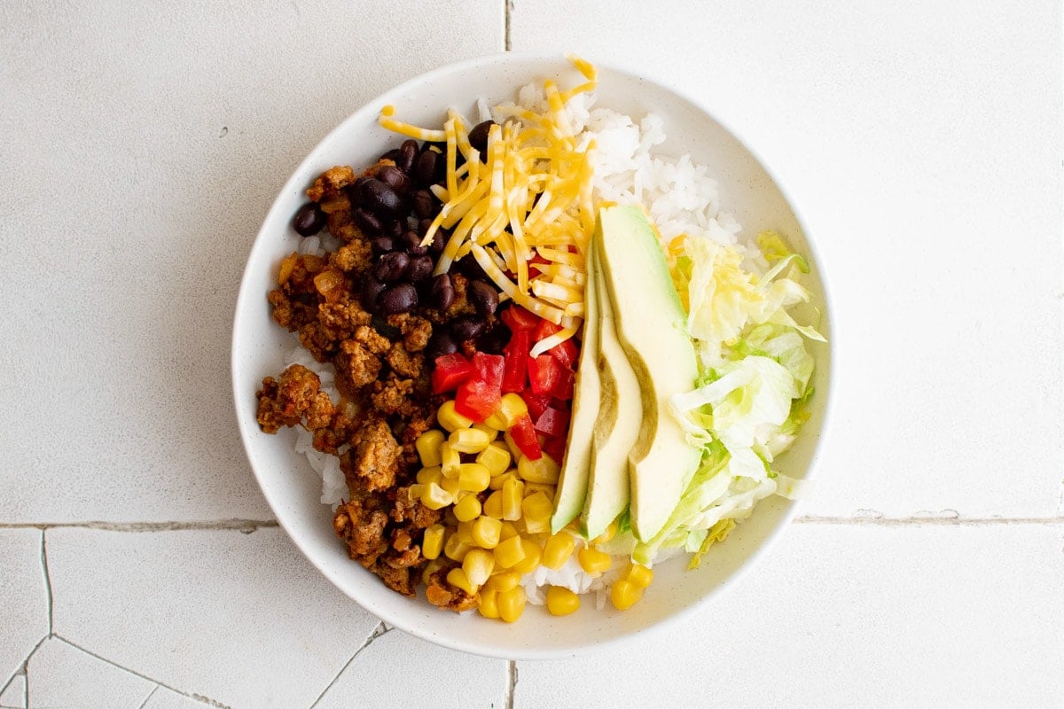 Taco bowl with rice, meat, black beans, tomatoes, corn and avocado.