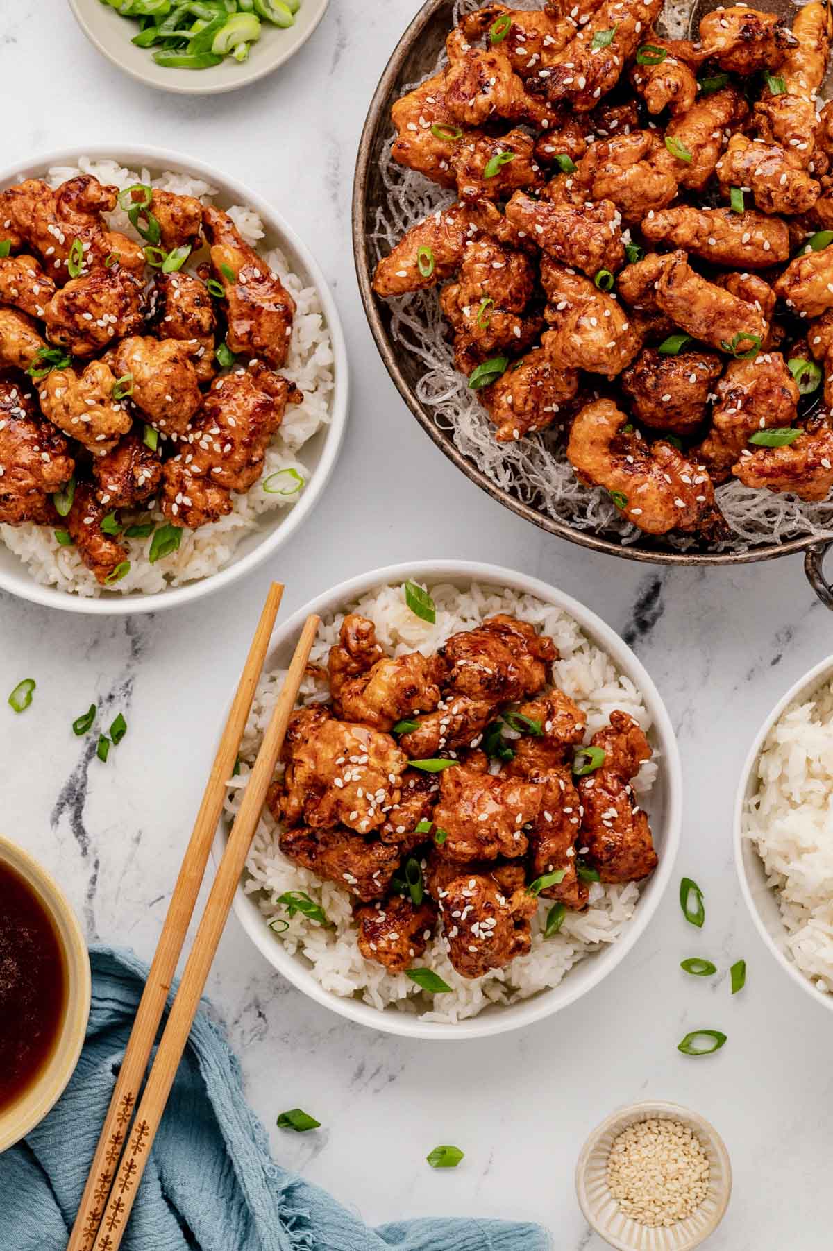 Honey chicken in bowls on top of rice with chopsticks.