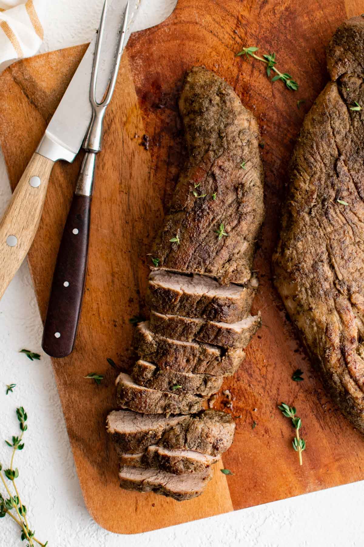 Sliced pork tenderloin on a cutting board, a sharp knife and a large fork.