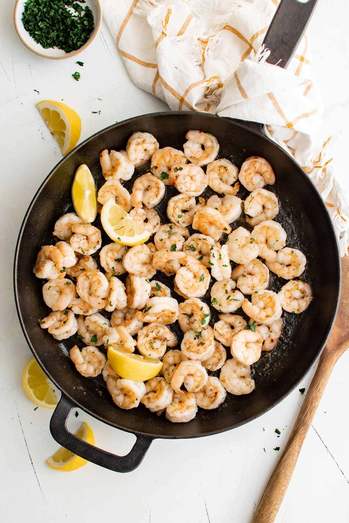 Pan seared shrimp in a large skillet, lemon wedges, a wooden spoon.