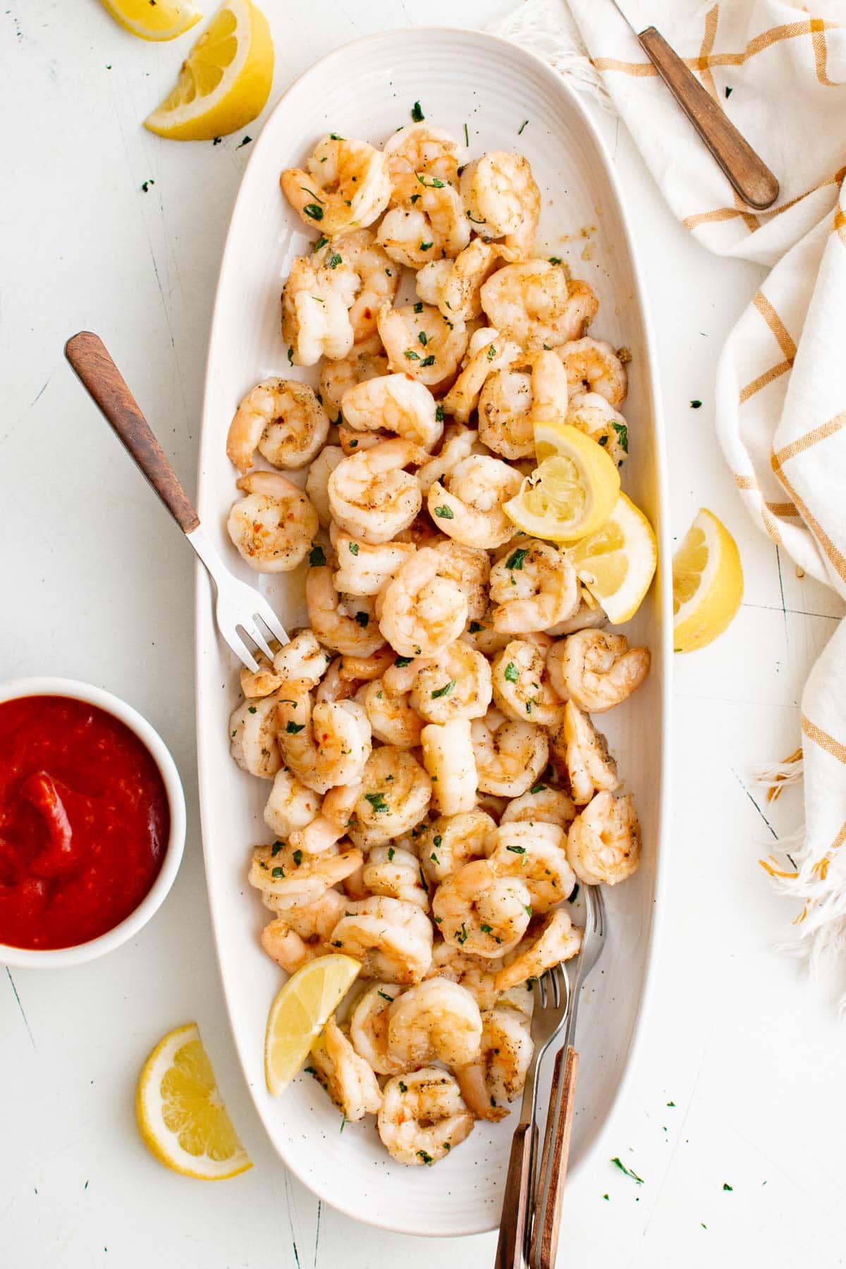 Pan seared shrimp on a white platter with a spoon and cocktail sauce.