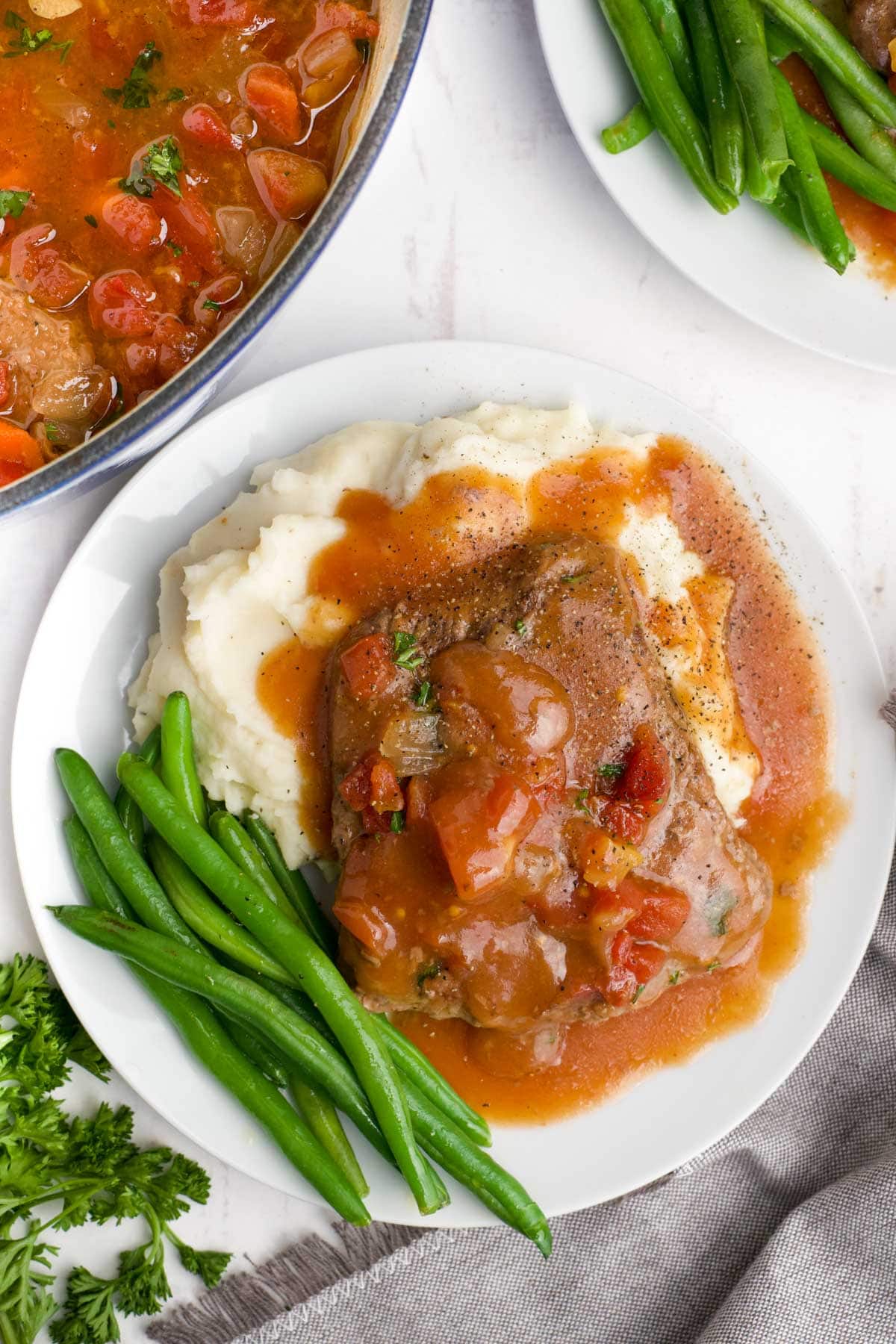 Swiss Steak with tomatoes served over mashed potatoes and with green beans.