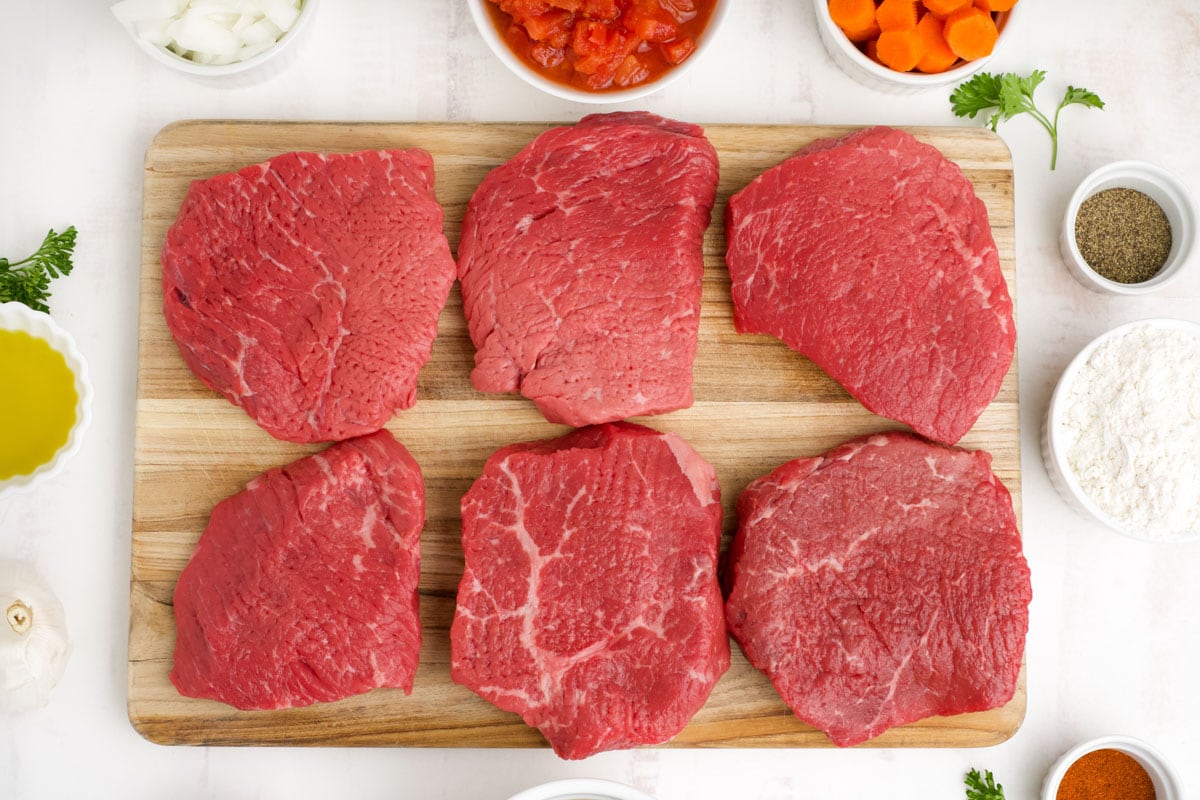 Thin steaks on a wood cutting board.