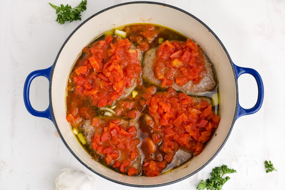 Diced tomatoes on top of steaks in a large dutch oven.