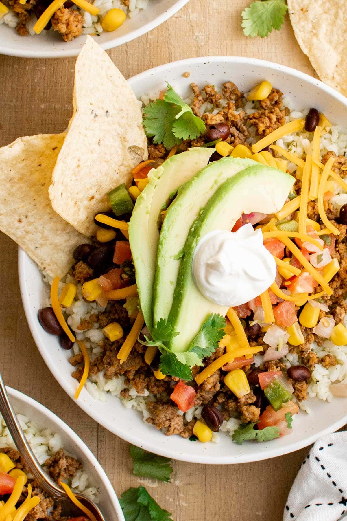 Close up of taco bowl with rice, meat, beans, cheese, avocado and tortilla chips.