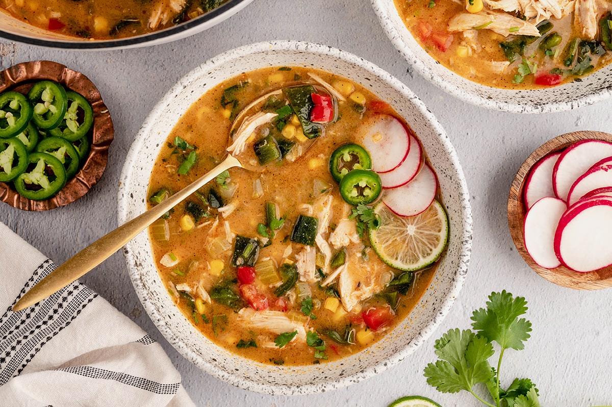 Chicken Poblano Soup in a bowl with a spoon and sliced radishes.