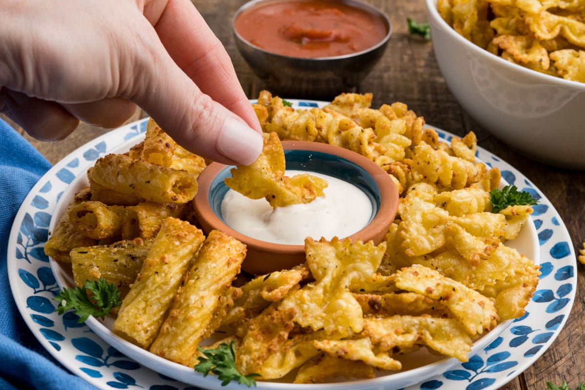 Pasta chips on a blue and white plate; a hand dipping a chip into ranch dressing.