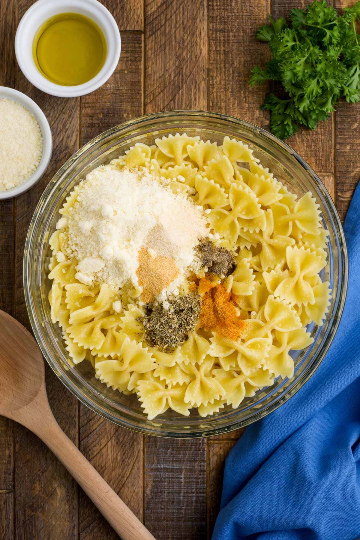 Cooked bowtie pasta, seasonings, parmesan cheese in a large bowl.