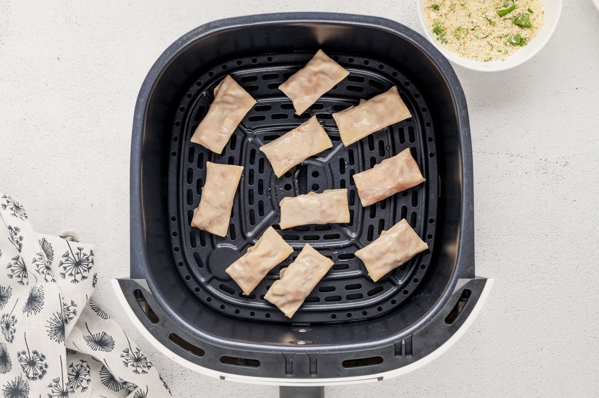 Uncooked pizza rolls in an air fryer basket.