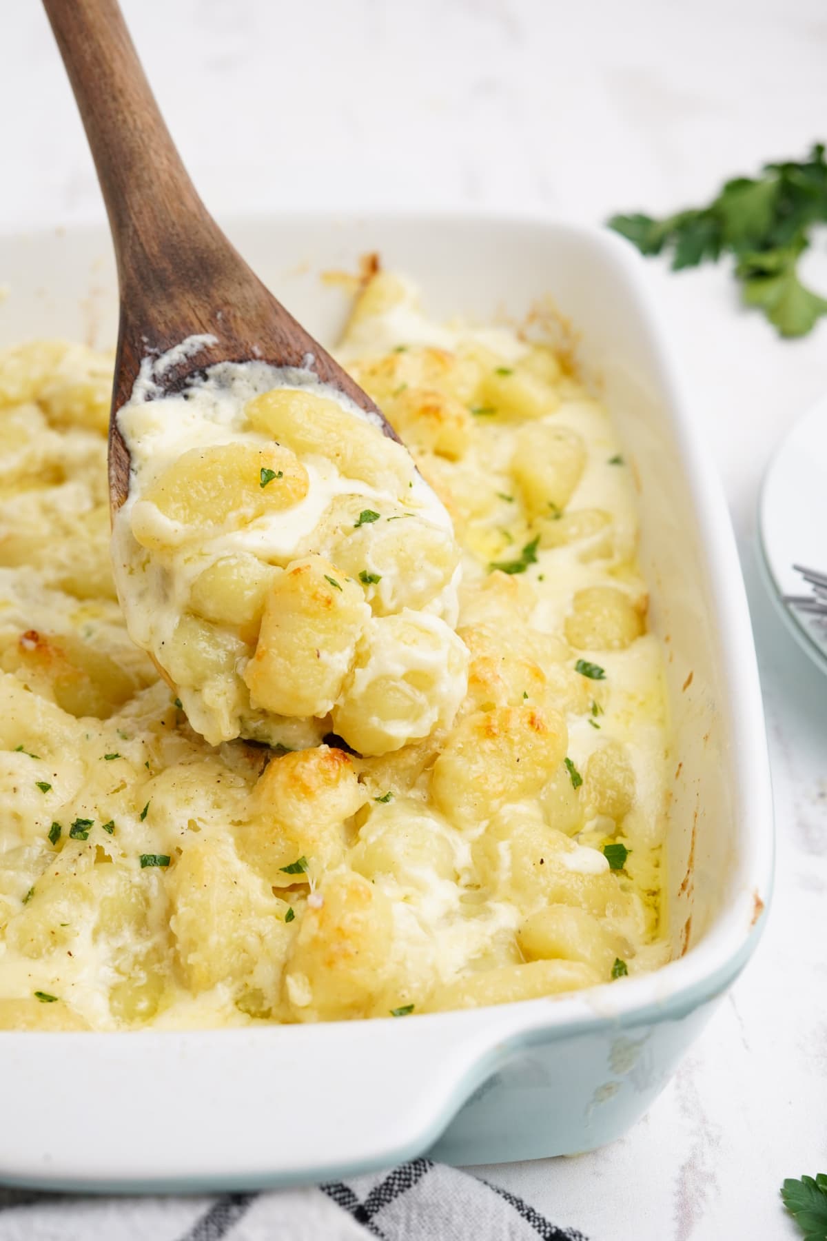 Gnocchi Alfredo with a wooden spoon in a casserole dish.